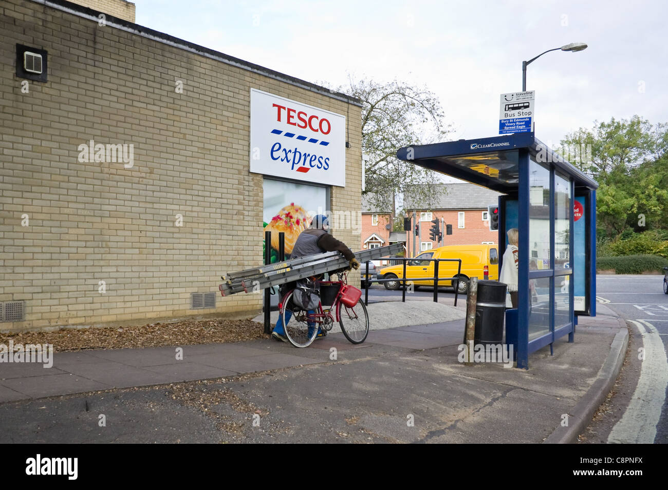 Un vieil homme pousse une échelle sur un vélo au-delà d'un magasin Tesco express, Bury St Edmunds, 2011 Banque D'Images