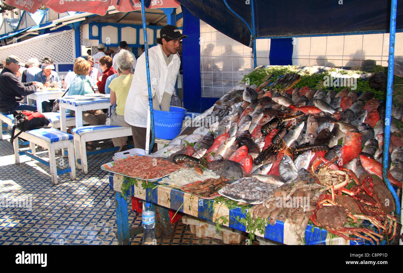 Les touristes manger au coin salon extérieur par le poisson frais des barbecues sur la promenade près du port à Essaouira, Maroc. Banque D'Images