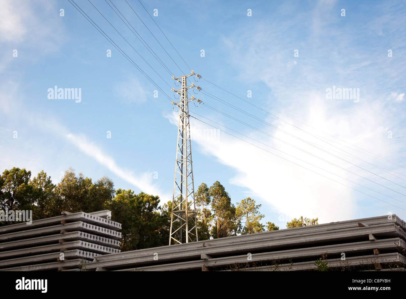 Pylône électrique à proximité d'une pile de barres de ciment contre ciel et forêt Banque D'Images