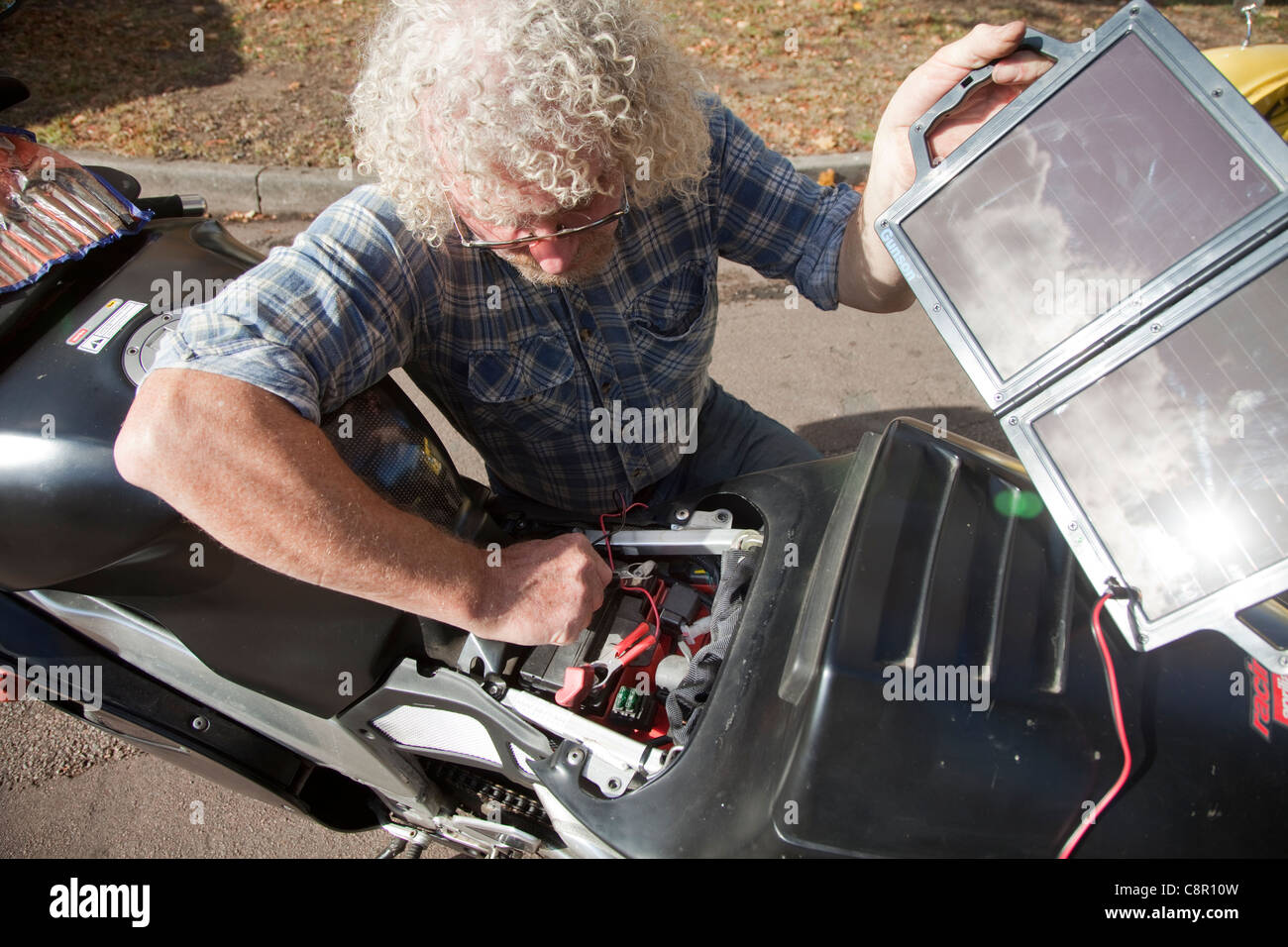 Un homme charge son vélo de moteur batterie avec un chargeur solaire UK Banque D'Images