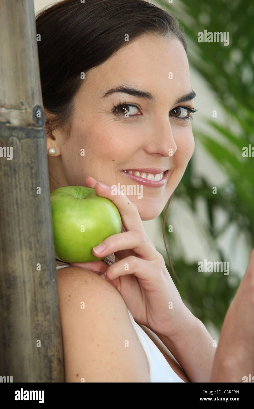 Une femme brune avec un apple appuyé contre un bâton de bambou Banque D'Images