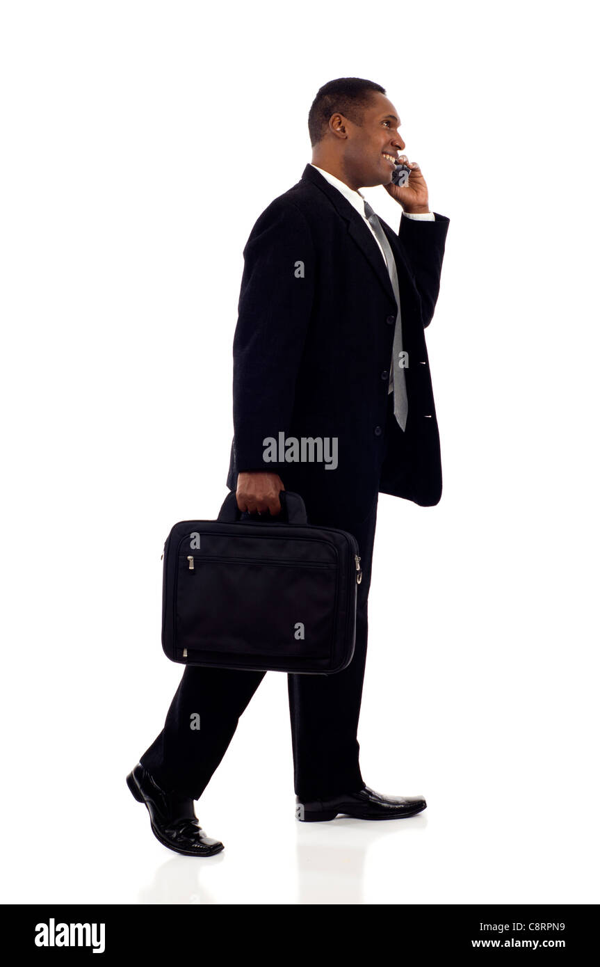 Happy black businessman talking on mobile phone while walking isolé sur fond blanc Banque D'Images