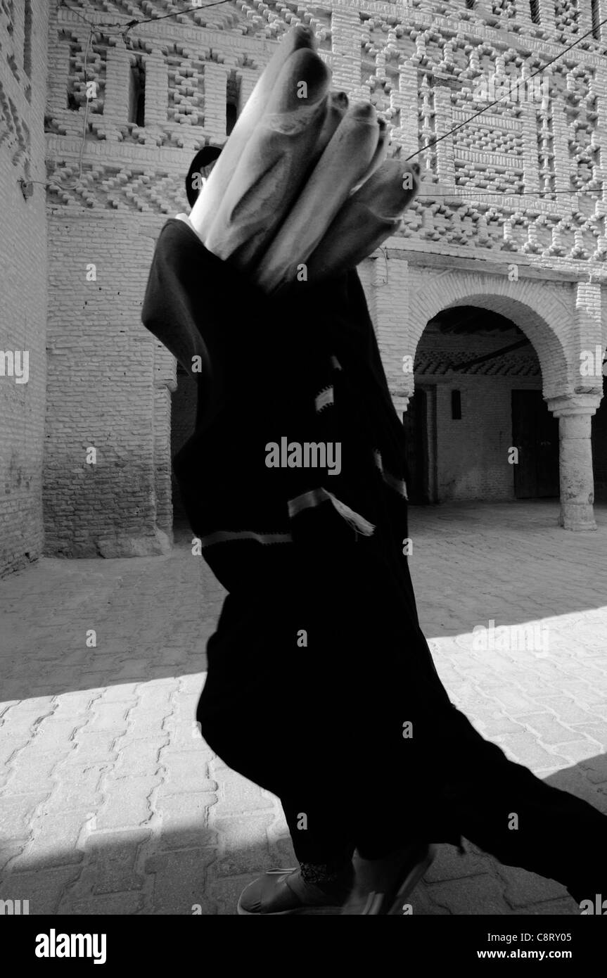 L'Afrique, Tunisie, Tozeur. Personne locale en portant une tenue traditionnelle berbère quelques baguettes à travers le vieux quartier de Tozeur. Banque D'Images