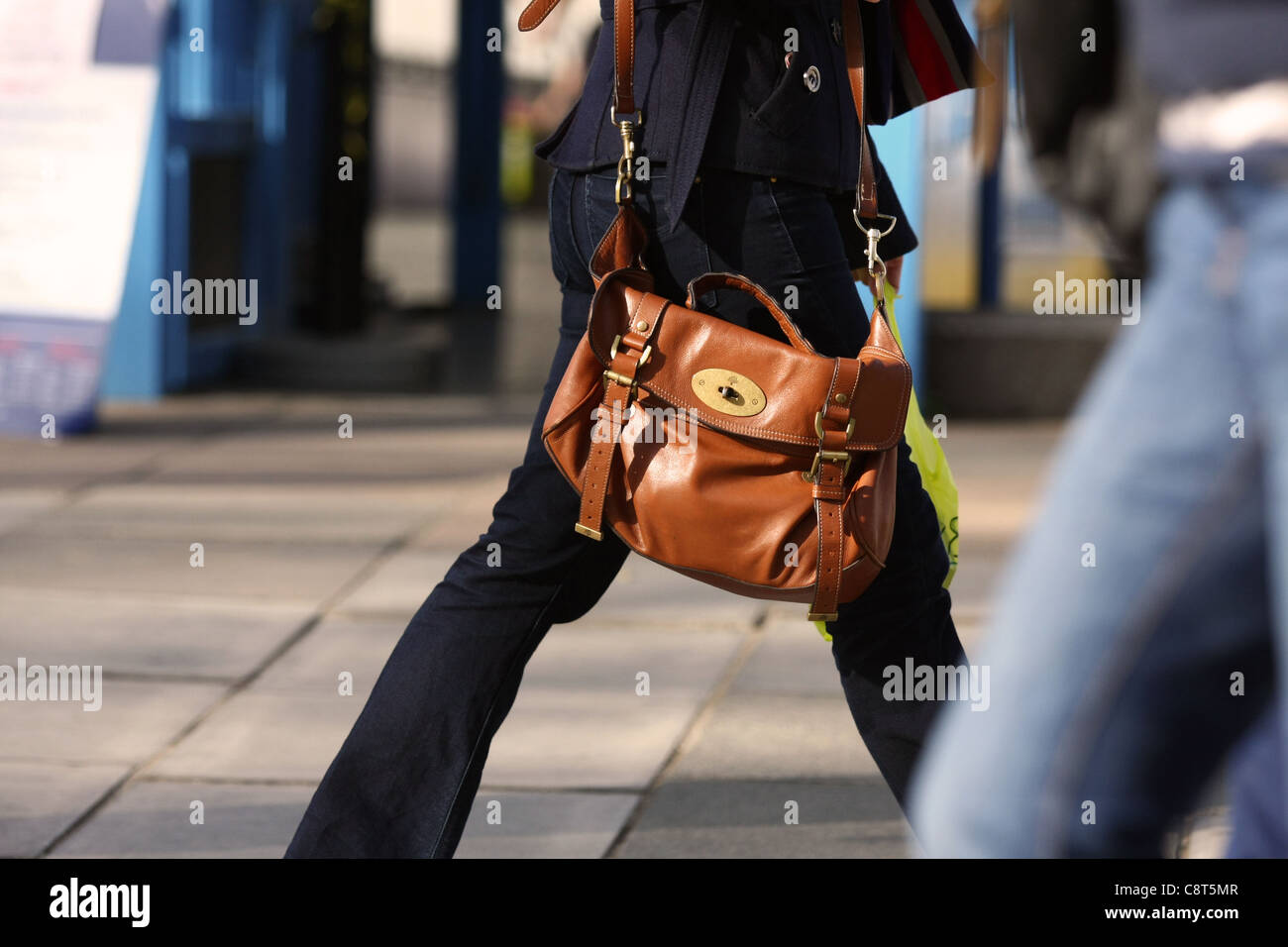 Une femme portant un sac à bandoulière brun comme elle marche le long de la  rue Photo Stock - Alamy