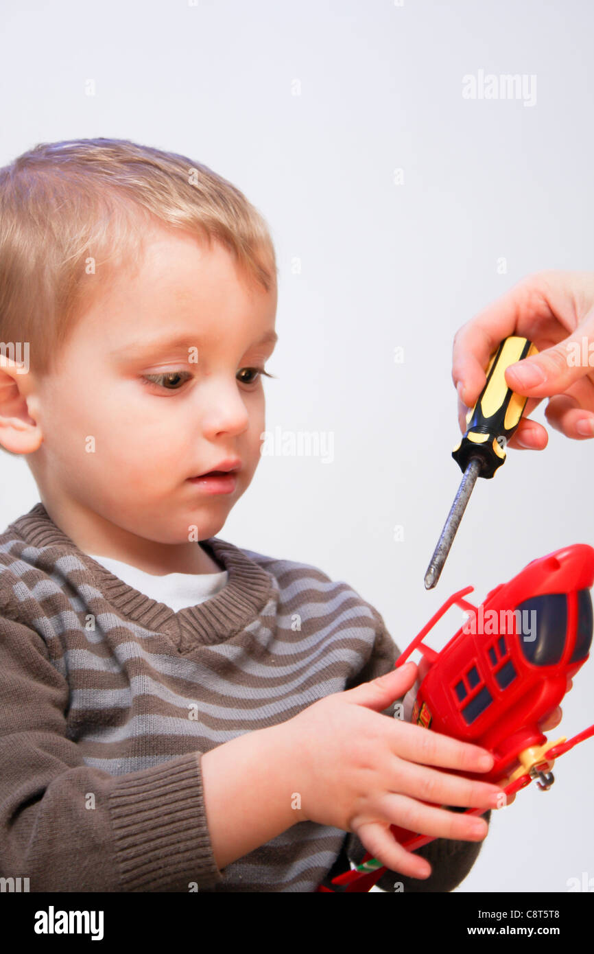 Un jeune homme enfant bébé garçon étant montré comment réparer son jouet brisé à l'aide d'un tournevis Banque D'Images