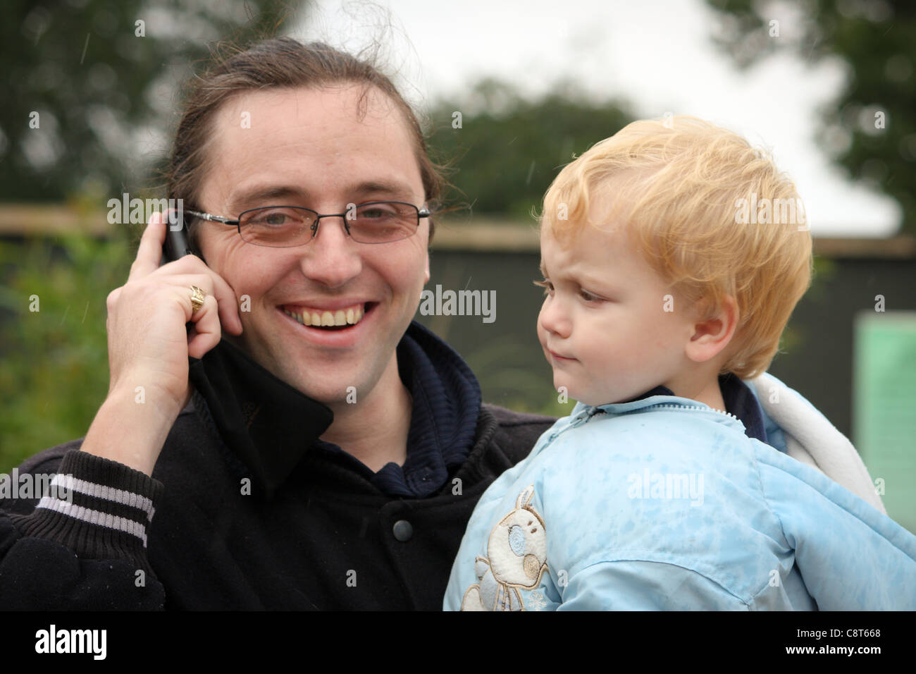 Un jeune homme enfant bébé garçon regarder son papa père qui est sourire et parler sur un téléphone mobile Banque D'Images