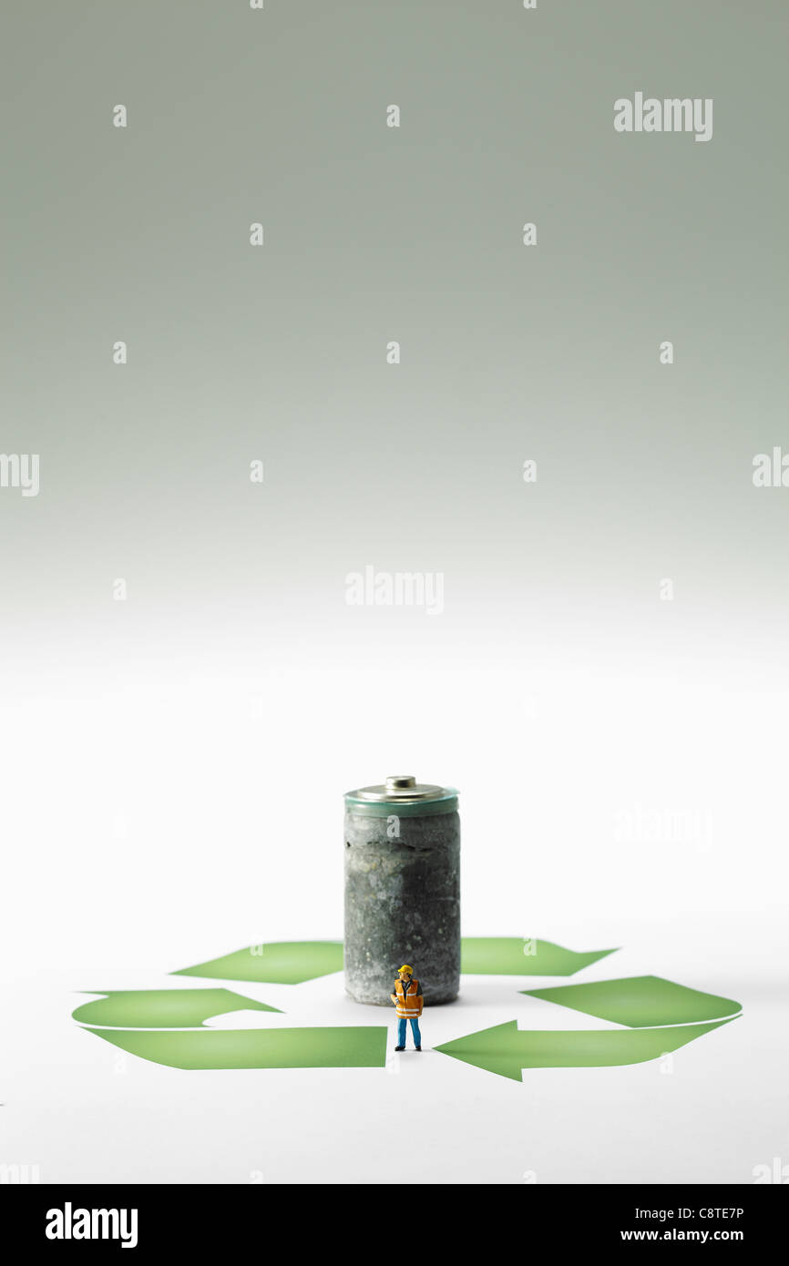 Petite figurine in front of rusty batterie et symbole de recyclage sur fond gris Banque D'Images