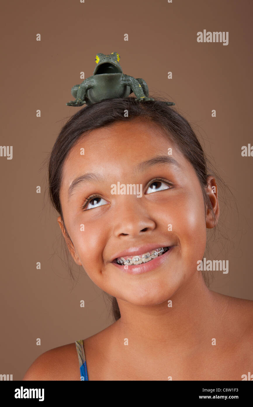 Studio Portrait of Girl balancing grenouille en plastique sur la tête Banque D'Images