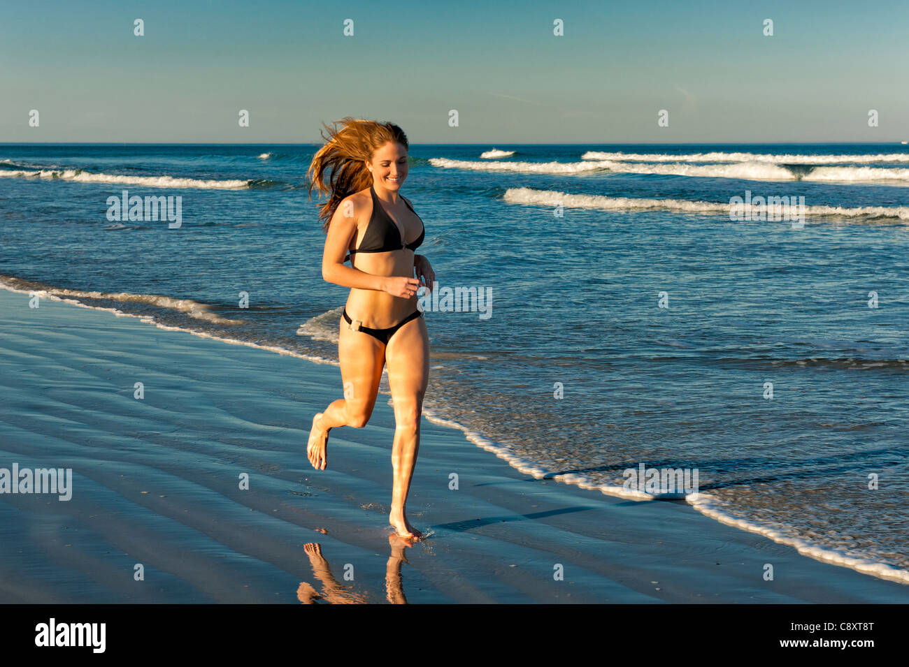 Très belle jeune femme blonde le jogging sur la plage, ses longs cheveux  volant dans le vent. La lumière de l'après-midi, haut de bikini noir 20s  Photo Stock - Alamy
