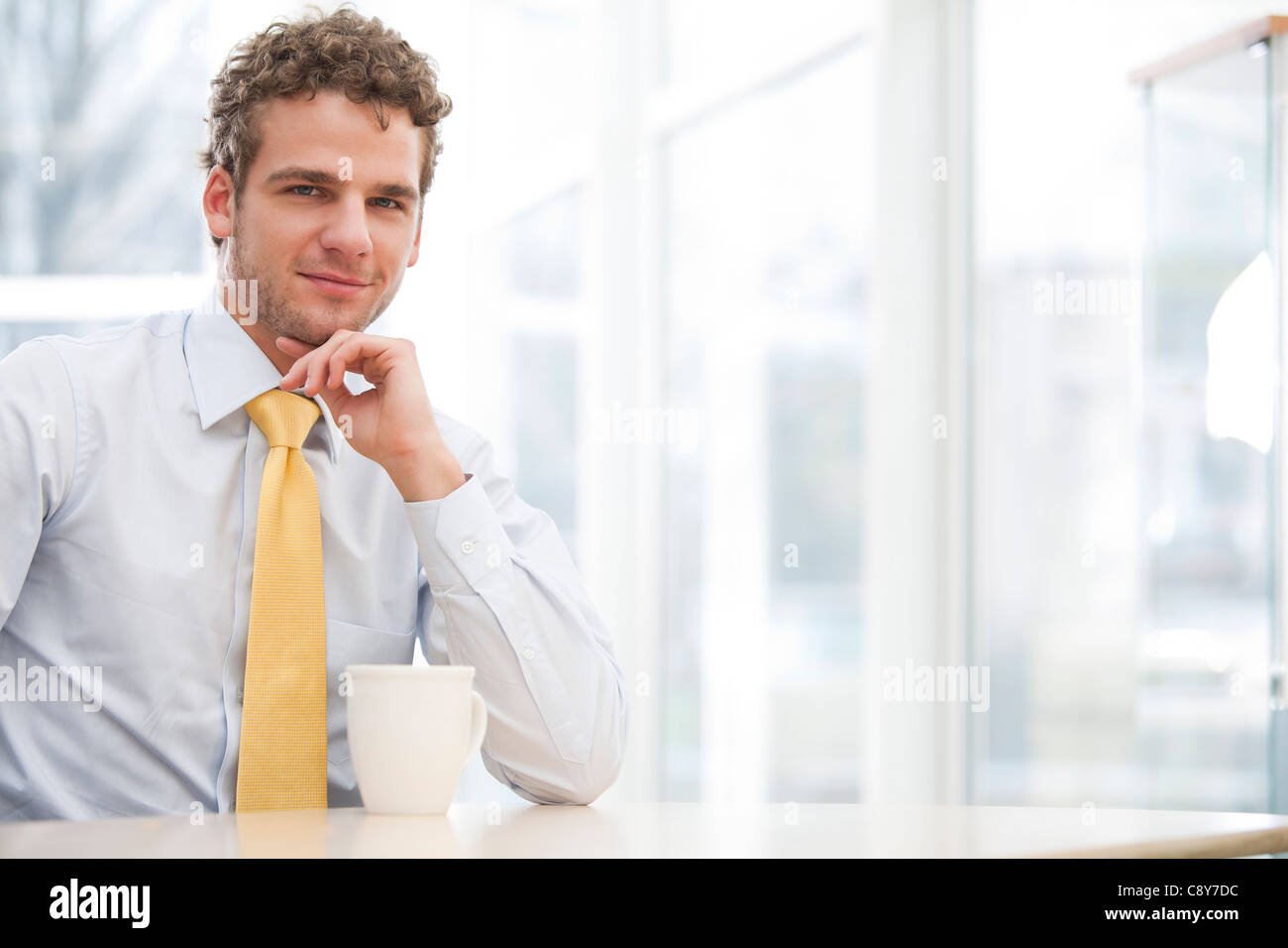 Portrait of young businessman sitting at desk with cup Banque D'Images