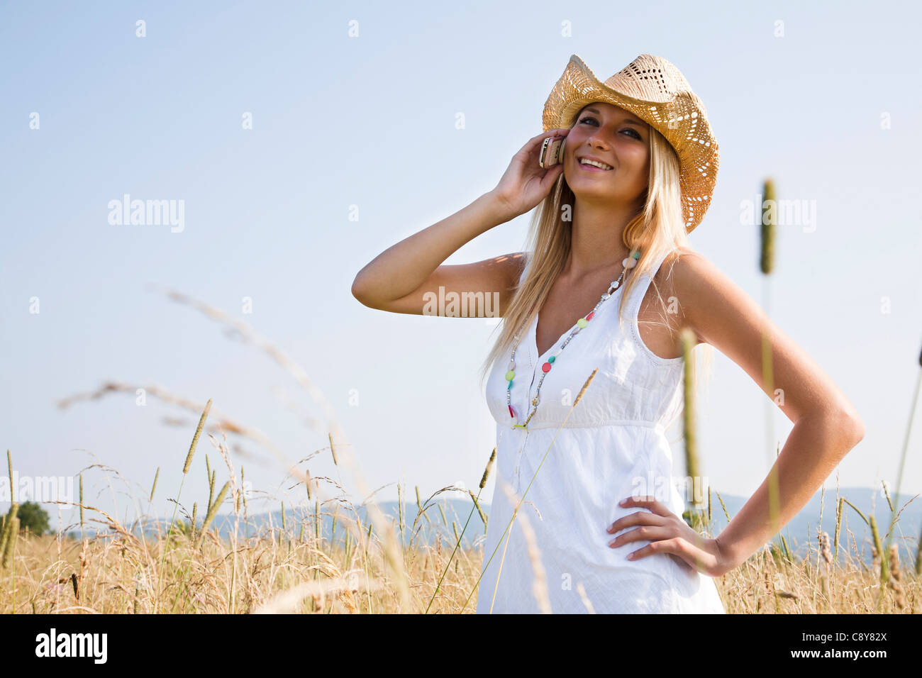 Portrait of young woman standing in field talking on mobile phone Banque D'Images