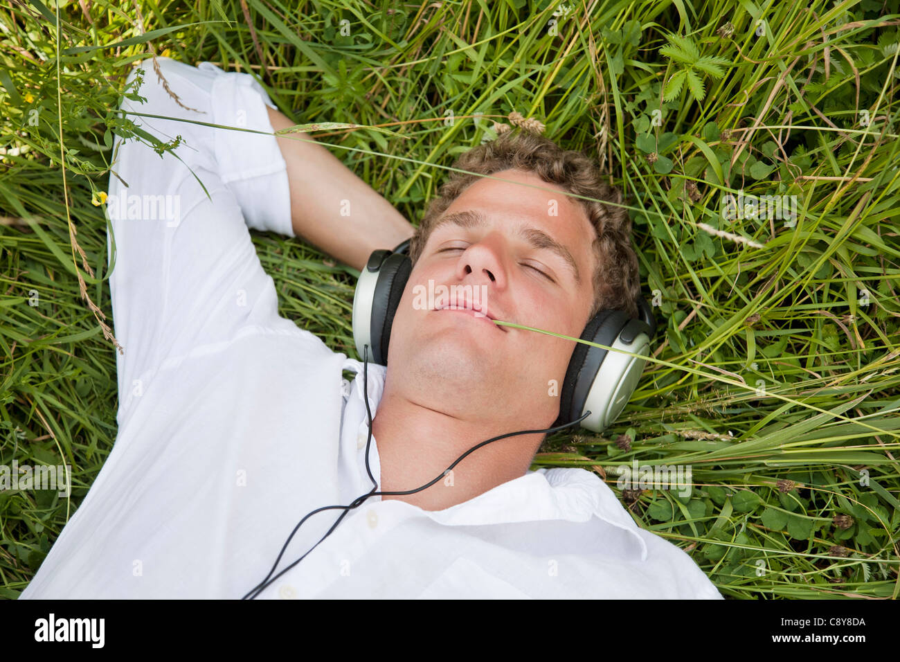 Portrait de jeune homme allongé dans l'herbe à écouter de la musique Banque D'Images