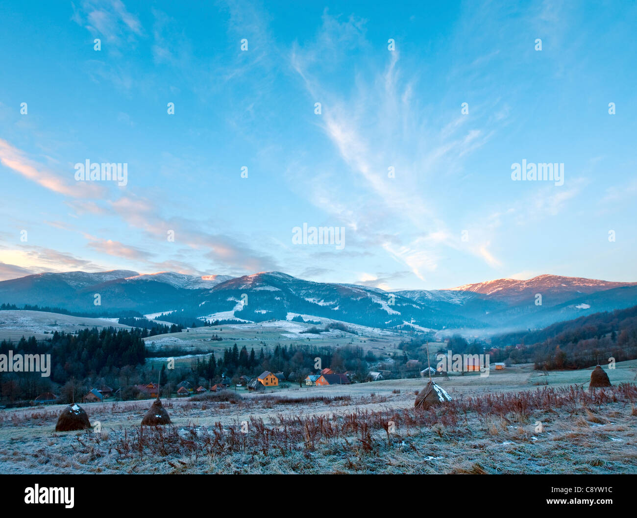 Premier gel d'automne sur les pâturages avec des bottes de foin et le lever du soleil dans les montagnes village Banque D'Images