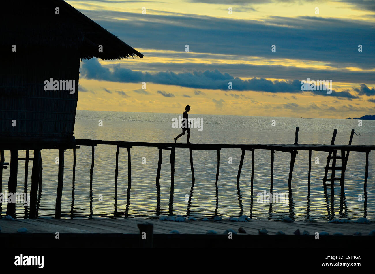 Lone woman walking on Jetty, coucher de soleil, mer, Kri Eco Resort, Raja Ampat îles de Papouasie occidentale dans l'océan Pacifique, l'Indonésie. Banque D'Images