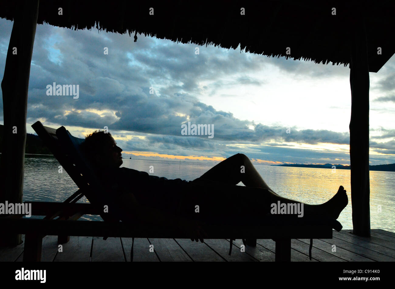 'Allongé sur le dos au coucher du soleil sur l'embarcadère de Kri Eco Resort, Raja Ampat îles de Papouasie occidentale dans l'océan Pacifique, l'Indonésie. Banque D'Images