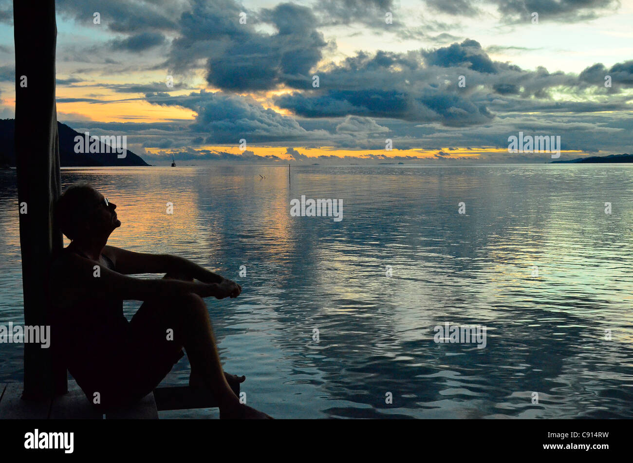 L'âge moyen de détente homme au coucher du soleil on jetty Kri, Raja Ampat îles de Papouasie occidentale dans l'océan Pacifique, l'Indonésie. Banque D'Images