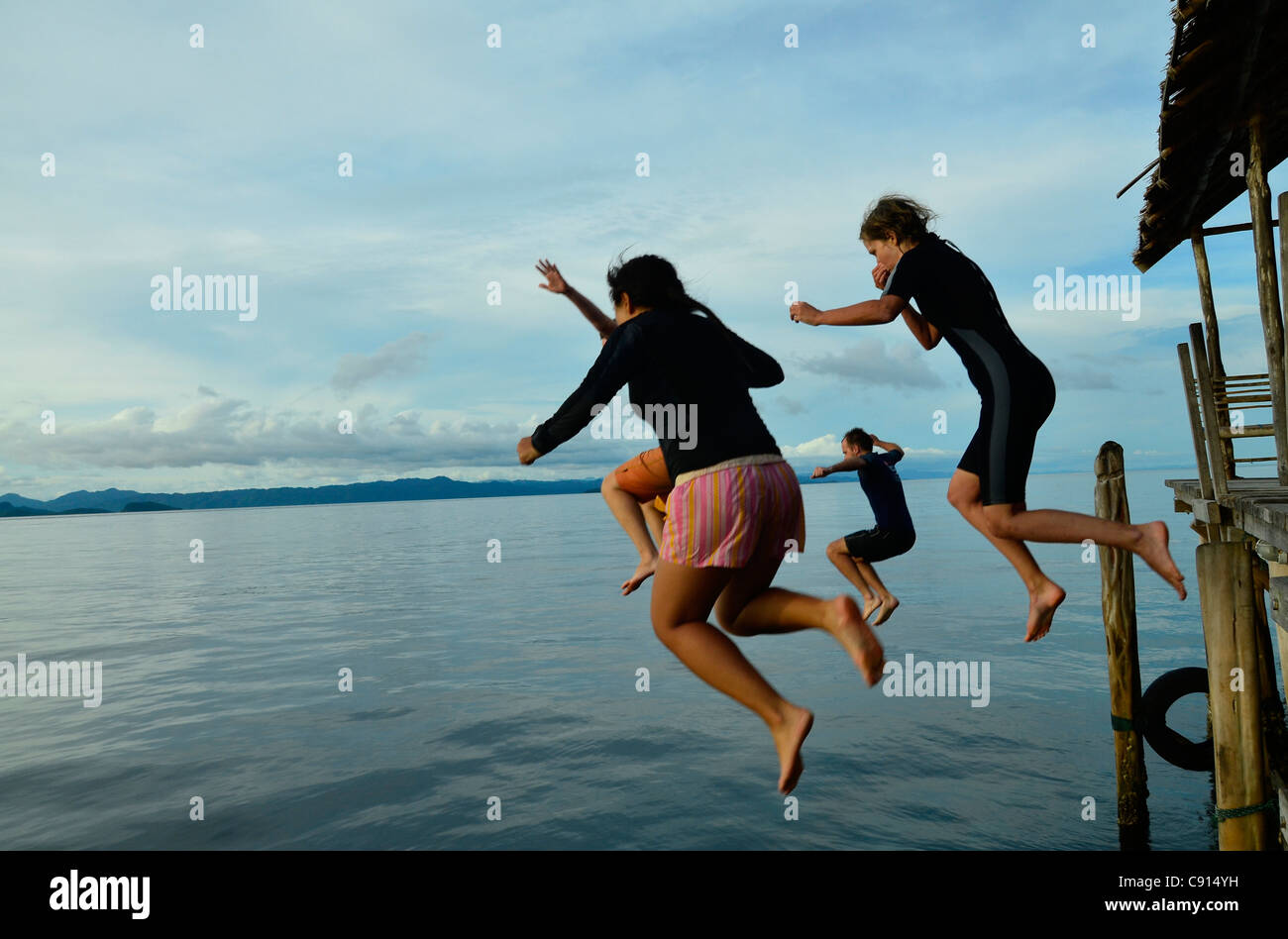 Les touristes sautent dans la mer depuis une jetée à Kri Eco Resort, Raja Ampat îles de Papouasie occidentale dans l'océan Pacifique, l'Indonésie. Banque D'Images