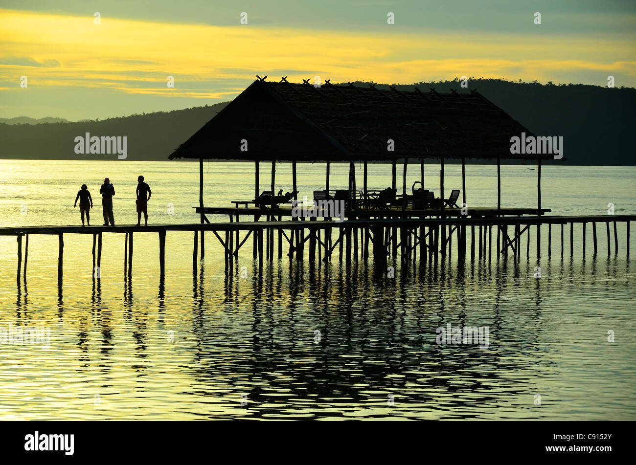 Trois touristes marcher sur pierre au coucher du soleil, Kri Eco Resort, Raja Ampat îles de Papouasie occidentale dans l'océan Pacifique, l'Indonésie. Banque D'Images