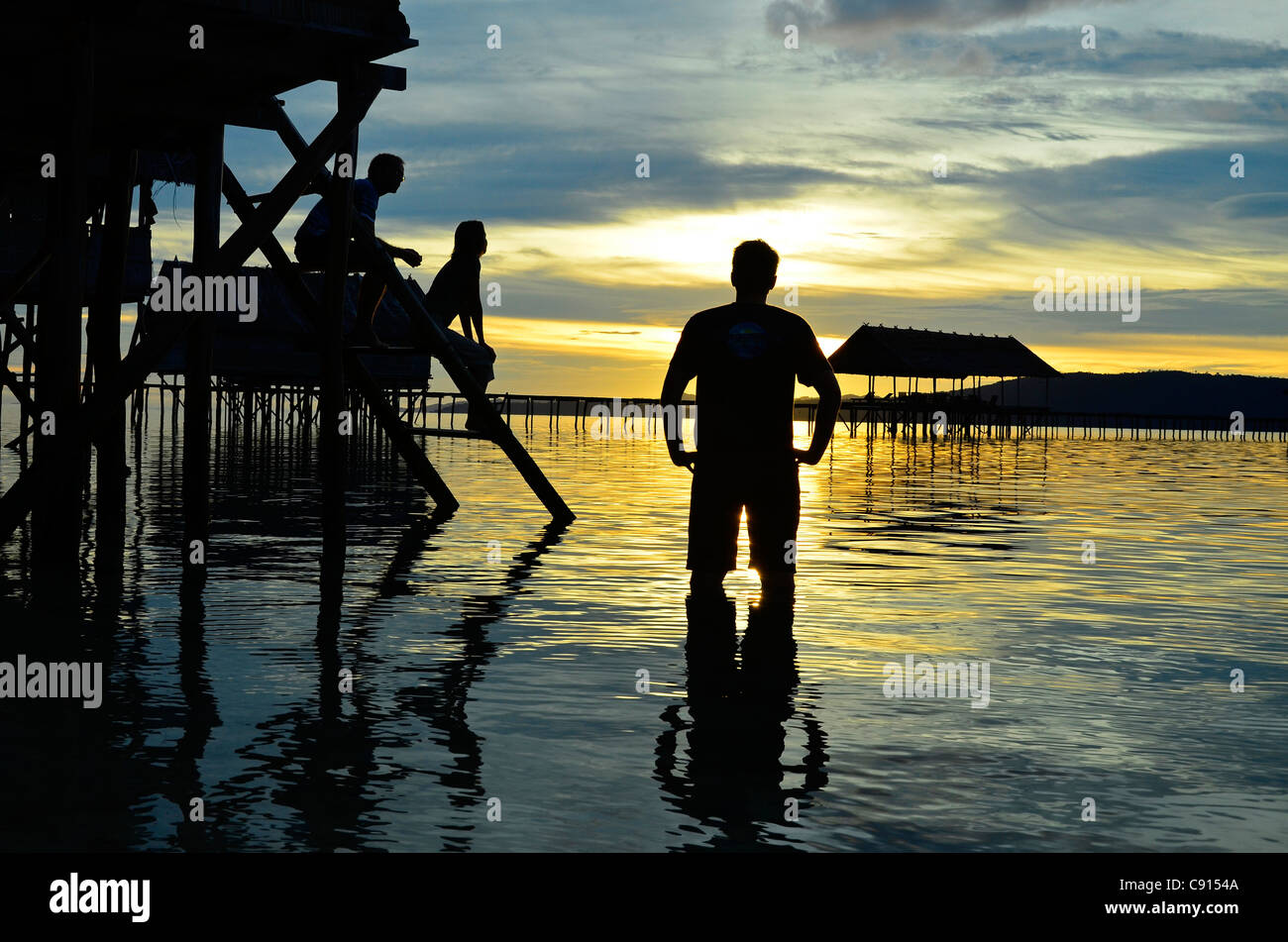 Deux hommes et femmes qui se profile au coucher du soleil, Kri Eco Resort, Raja Ampat îles de Papouasie occidentale dans l'océan Pacifique, l'Indonésie. Banque D'Images