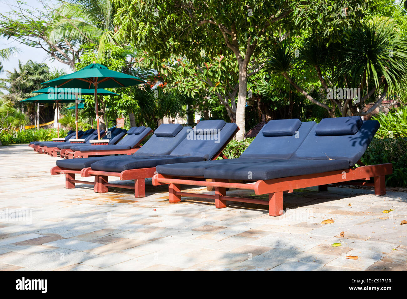 Des chaises longues et des parasols près de la piscine dans un jardin tropical Banque D'Images