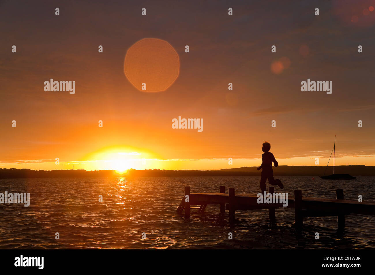 Boy running on wooden dock au coucher du soleil Banque D'Images