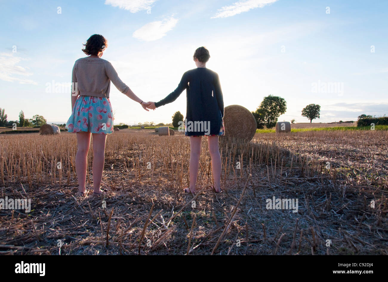 Girls holding hands in hay field Banque D'Images