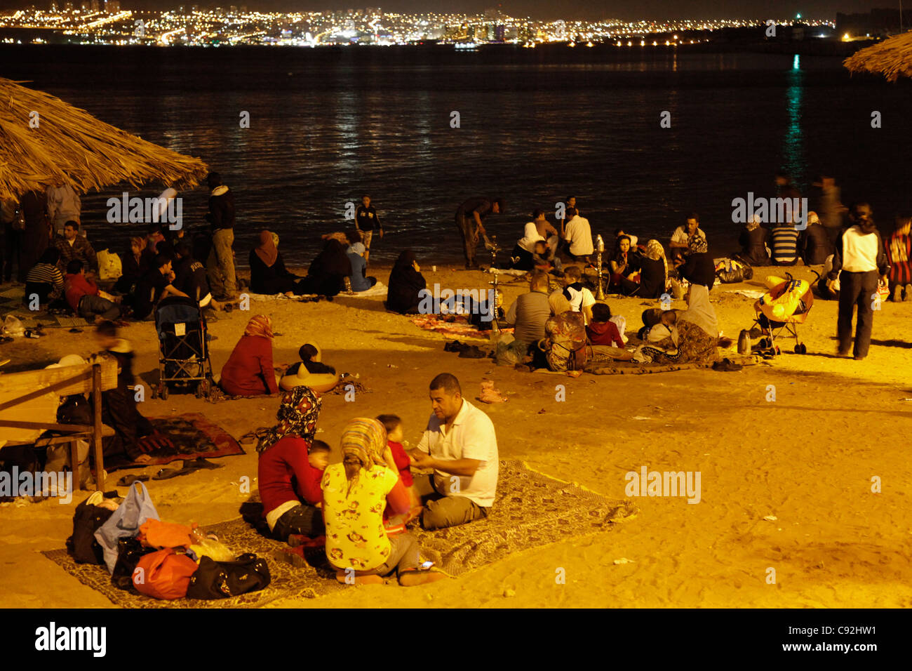 Les gens sur la plage publique de nuit avec Eilat en arrière-plan, Aqaba, Jordanie. Banque D'Images
