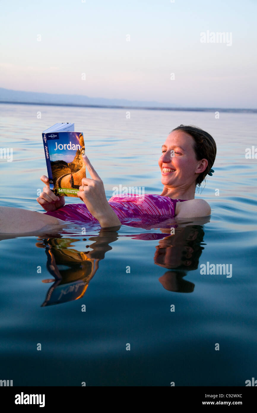 Touriste / girl lit le guide de voyage Lonely Planet en Jordanie tout en flottant / un flotteur sur l'eau salée de la Mer Morte Banque D'Images
