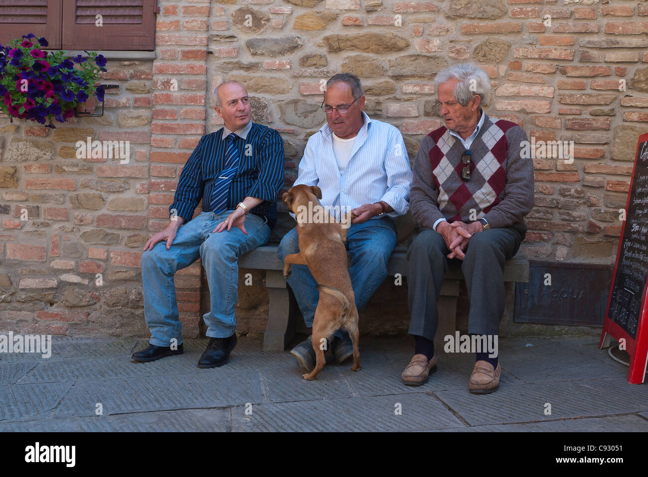 Adultes plus âgés de trois hommes italiens s'asseoir sur un banc partir de flatter un chien à Panicale, Italie. Banque D'Images