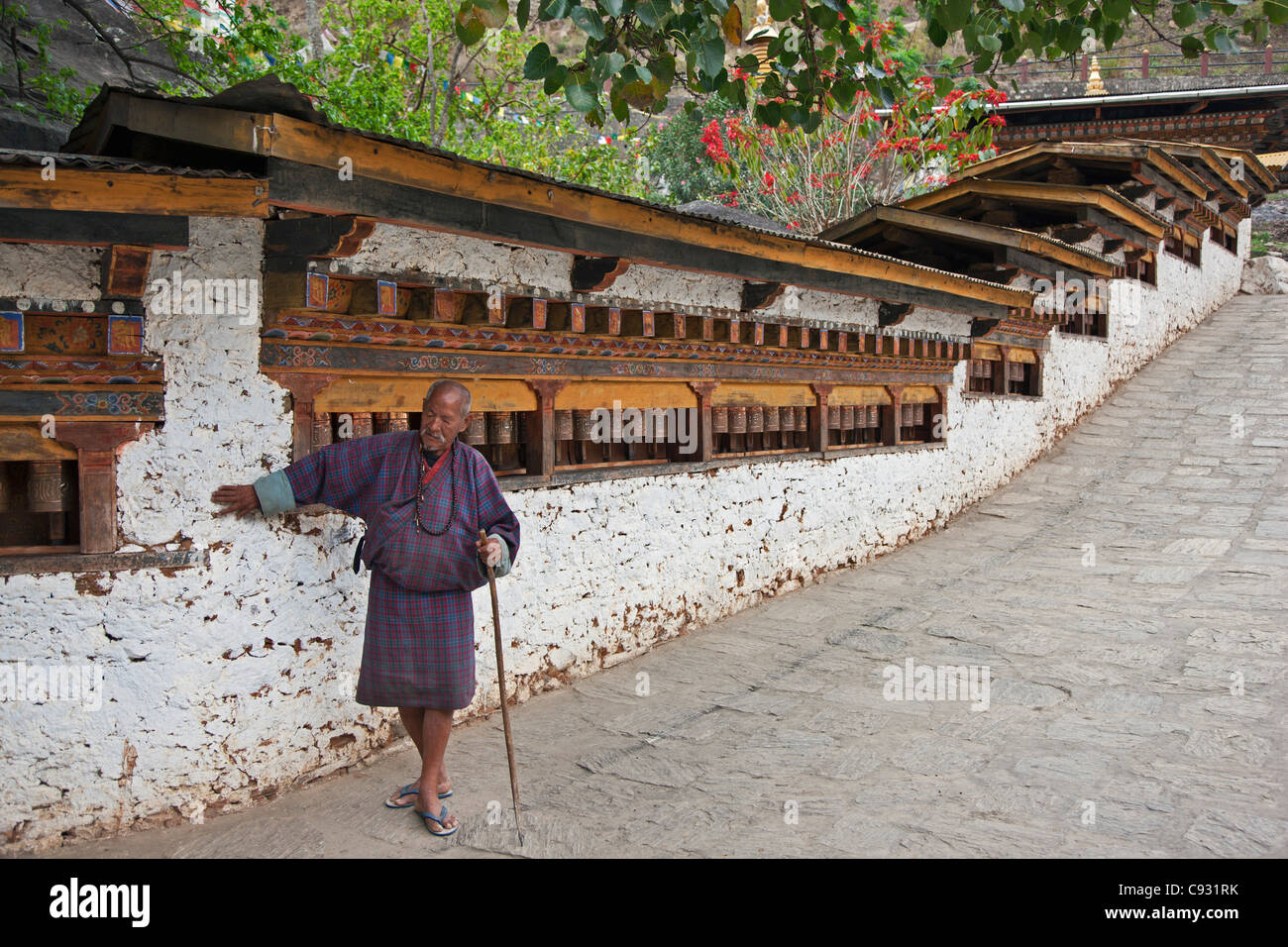 Un homme aveugle tourne une longue ligne d'airain roues de prière comme il marmonne une invocation de divinités protectrices à Gom Kora monastère. Banque D'Images
