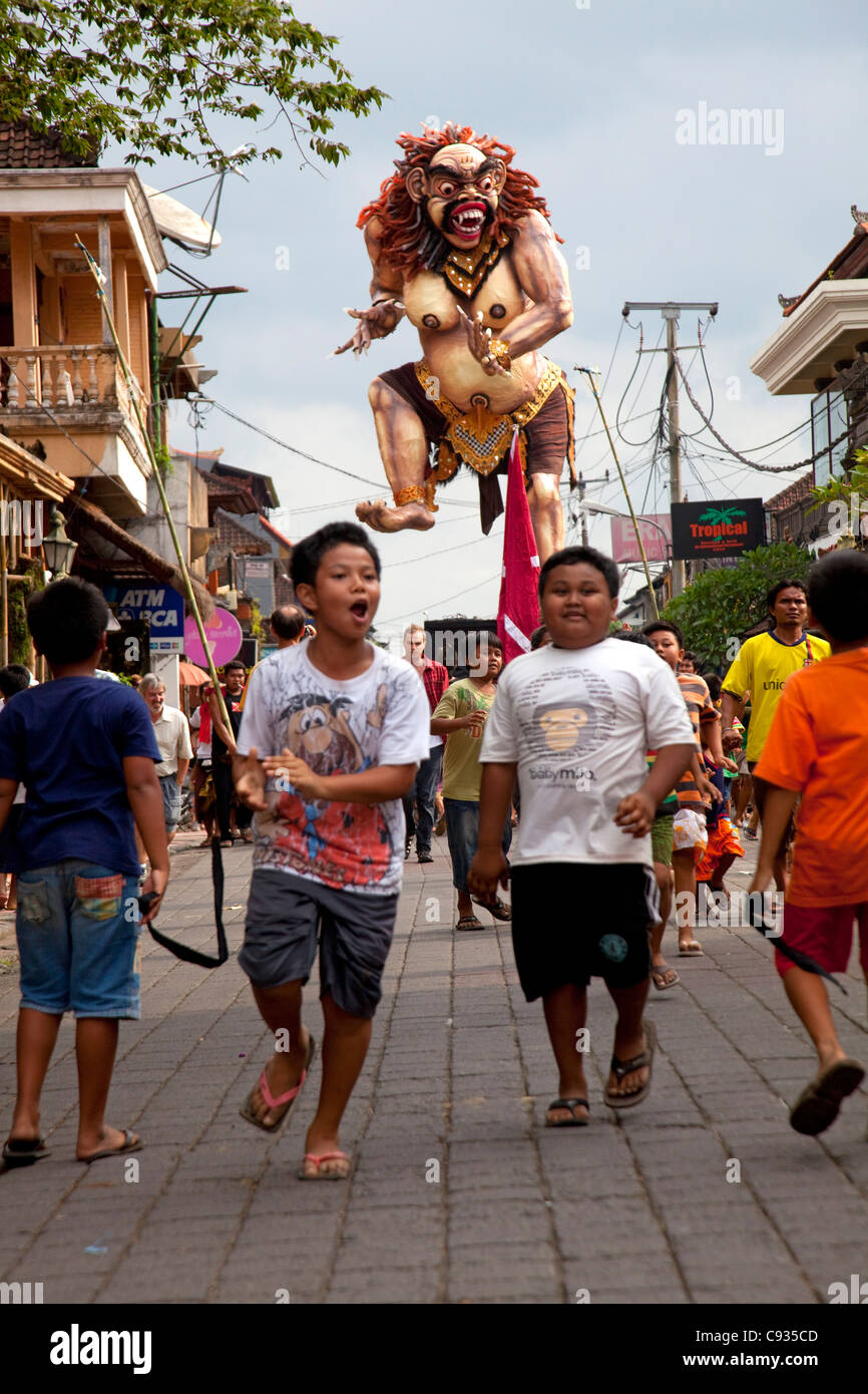 Bali, Ubud. Les enfants courir dans les rues de l'effrayant-Ogoh ogoh monters dans le cadre de la fête du Nouvel An. Banque D'Images