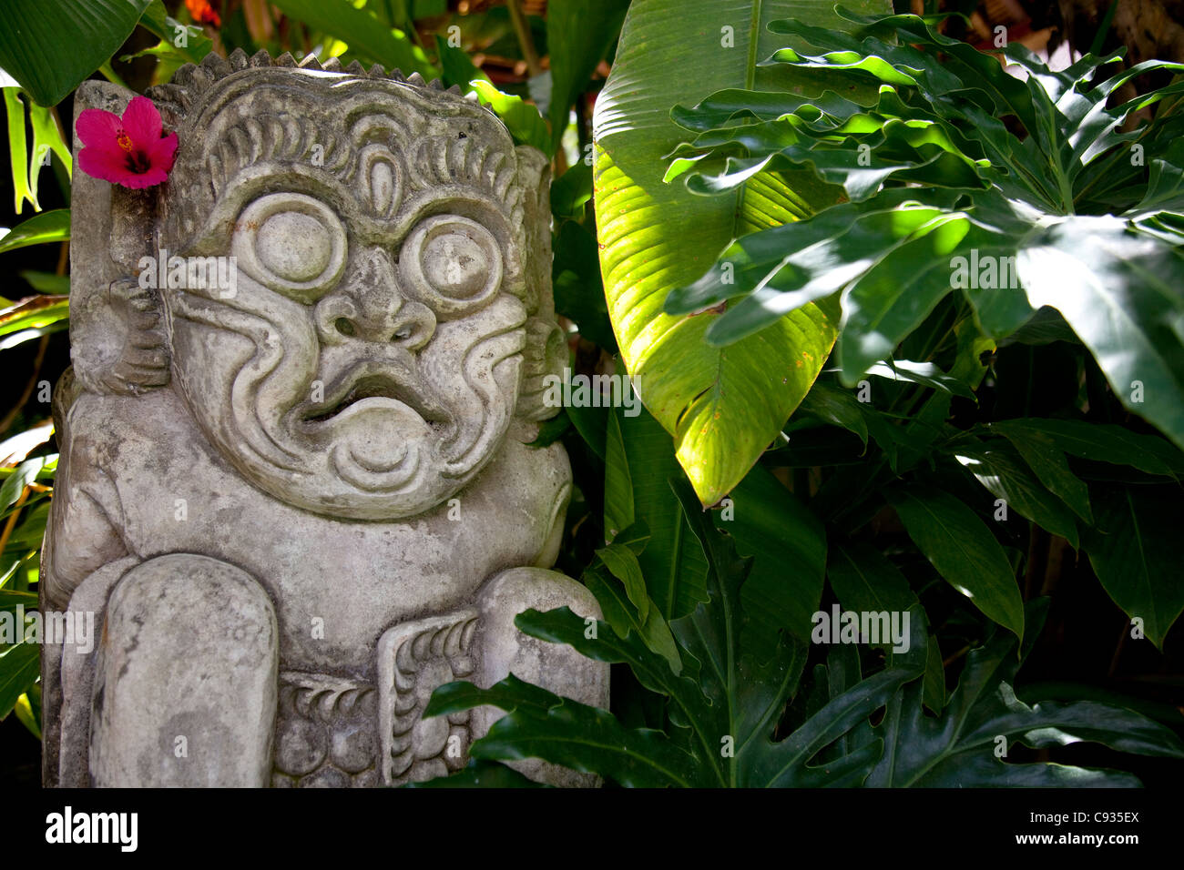 Bali, Ubud. Une sculpture en pierre, ornée d'une fleur d'hibiscus, se trouve dans des jardins tropicaux. Banque D'Images