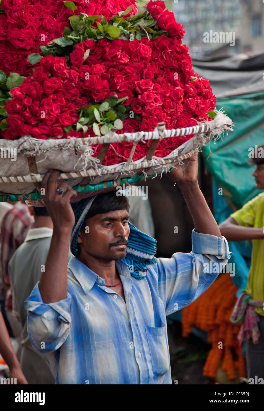 Un porteur porte paniers de roses rouges dans les Mullik Ghat marché aux fleurs près de Howrah Bridge. Banque D'Images