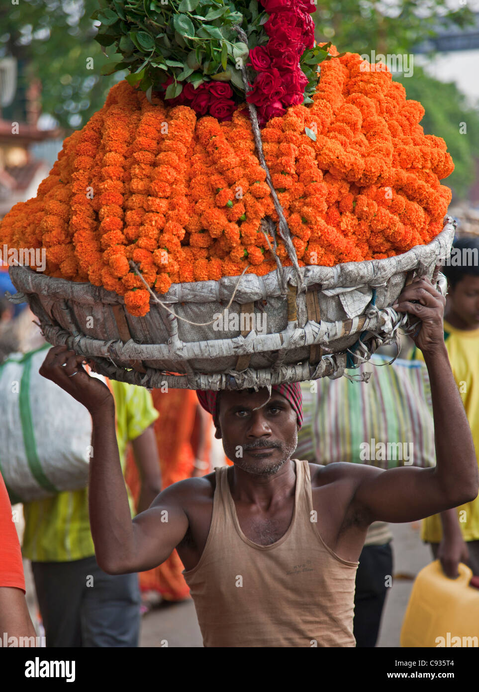 Un homme porte une headload d'œillets et de roses dans les Mullik Ghat marché aux fleurs près de Howrah Bridge. Banque D'Images