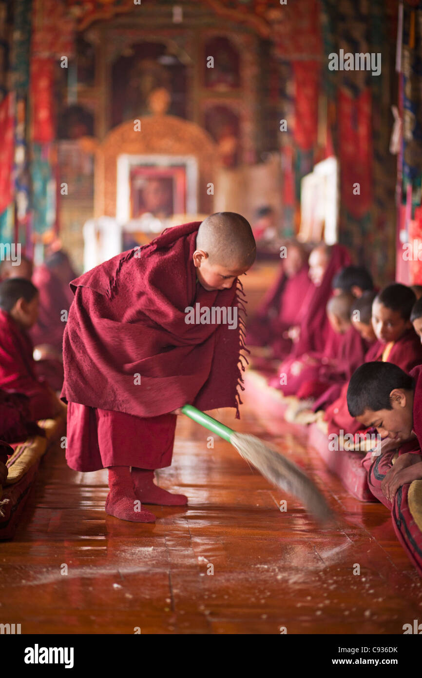 L'Inde, le Ladakh, Thiksey. Jeune moine novice balayant la tsampa miettes aux prières du matin ou puja, Monastère de Thiksey. Banque D'Images