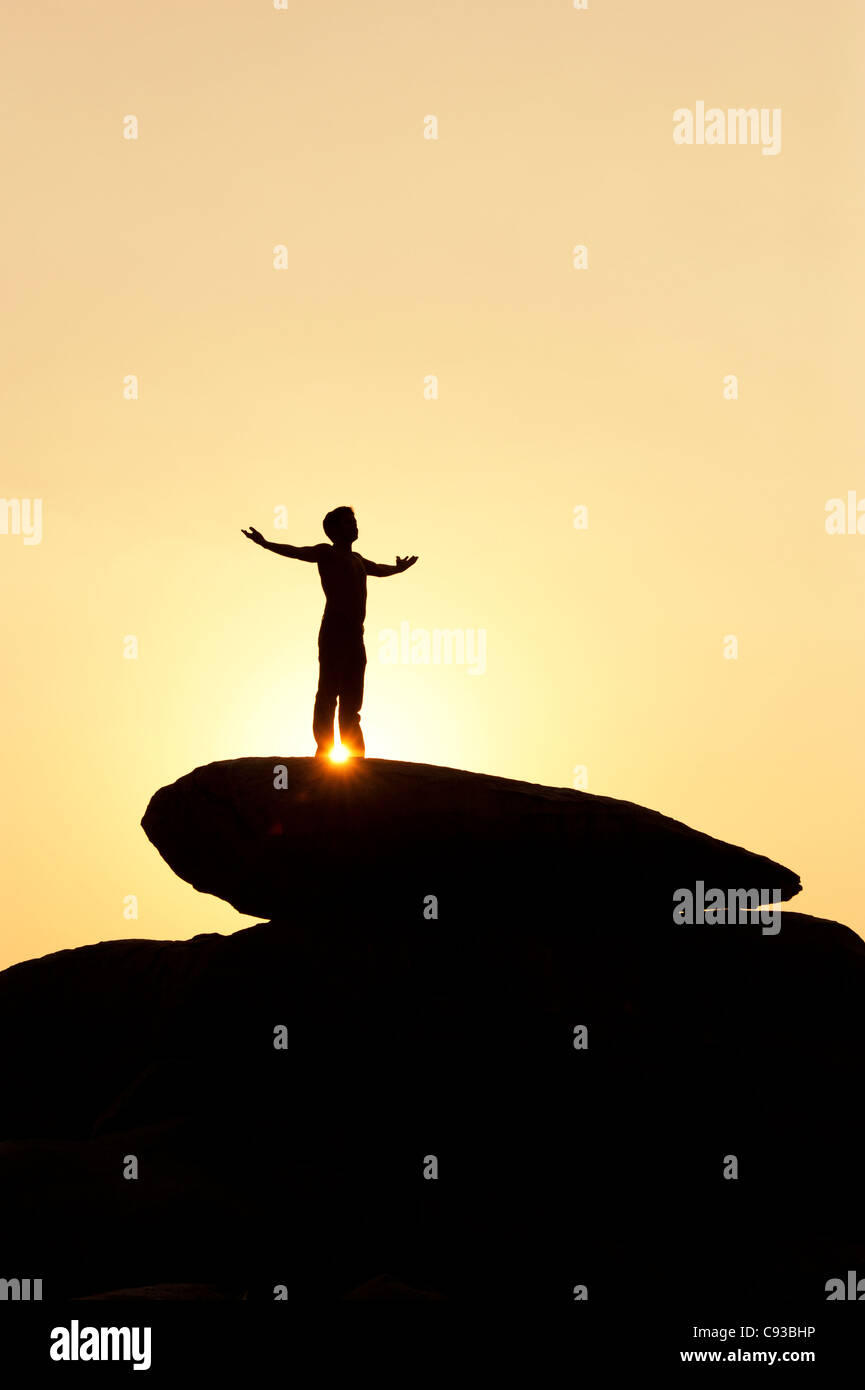 Homme debout sur un rocher qui englobe le soleil. Silhouette. L'Inde Banque D'Images