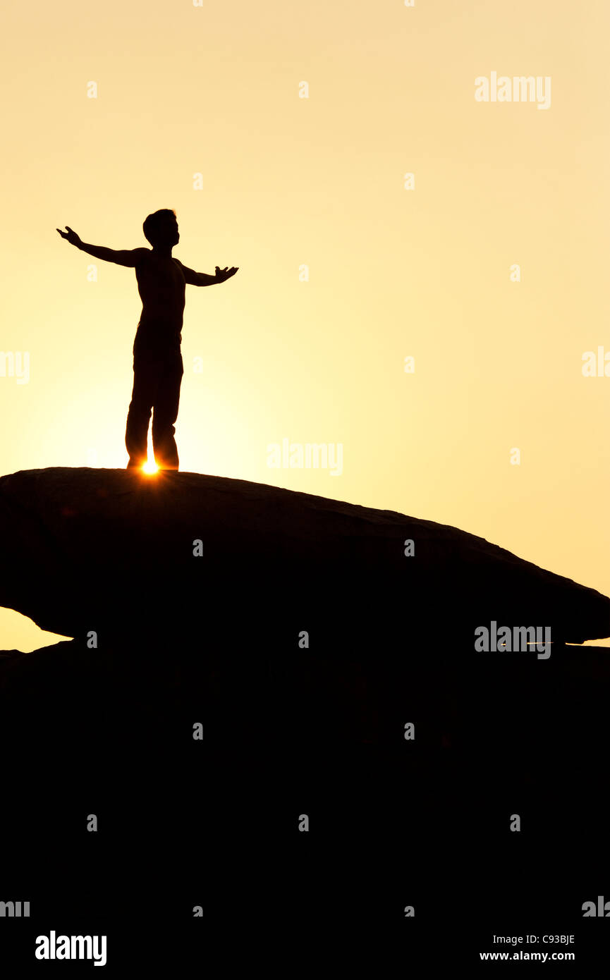 Homme debout sur un rocher qui englobe le soleil. Silhouette. L'Inde Banque D'Images