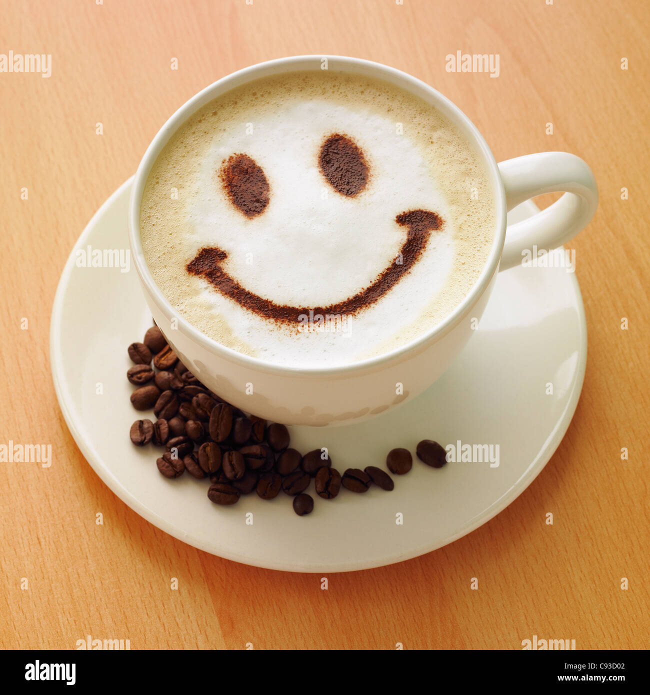 Cappuccino avec un chocolat en poudre smiley face sur le dessus et les grains de café sur la soucoupe. Banque D'Images