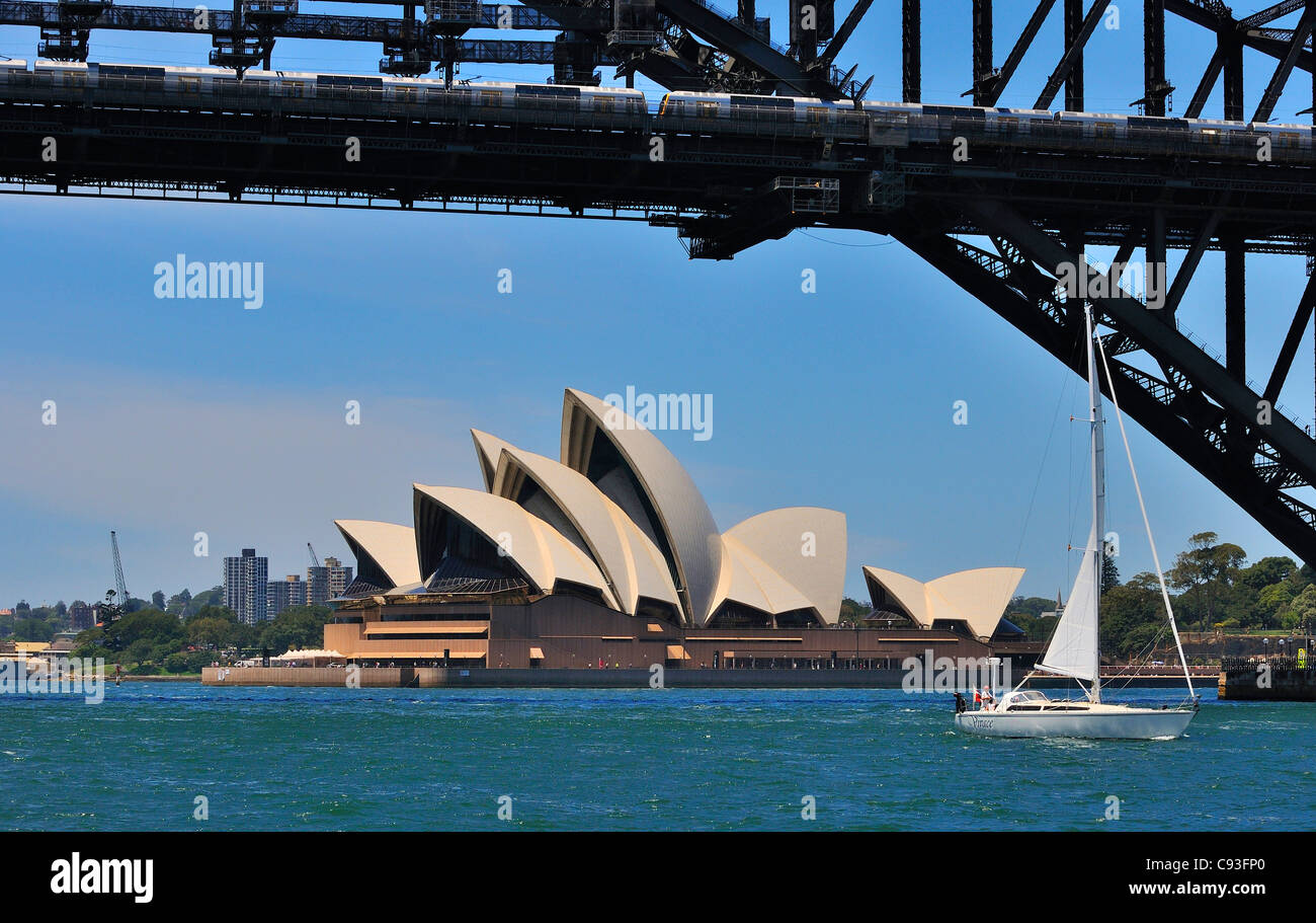 Vue sur le bord de l'eau depuis le ferry vers l'emblématique Opéra de Sydney avec un yacht naviguant sous le pont du port de Sydney, en Australie Banque D'Images
