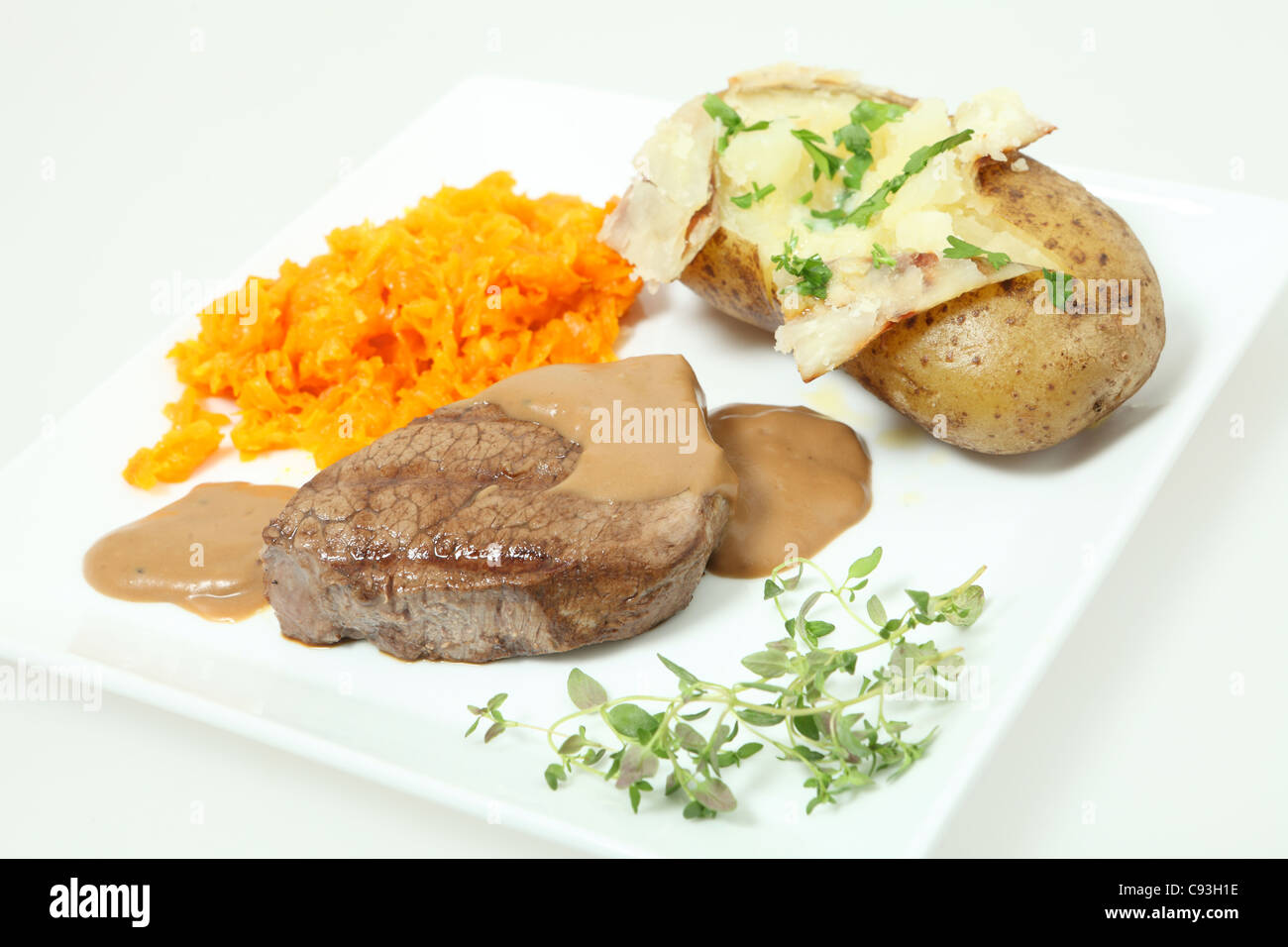 Un filet mignon de filet de boeuf servi avec des carottes braisées et une pomme de terre cuite au four. Garnir de persil et thym Banque D'Images