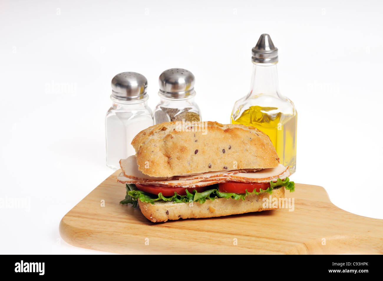 Poulet à la tomate et laitue sandwich dans un rouleau sur le bois à découper avec les condiments de sel, poivre et huile d'olive on white Banque D'Images