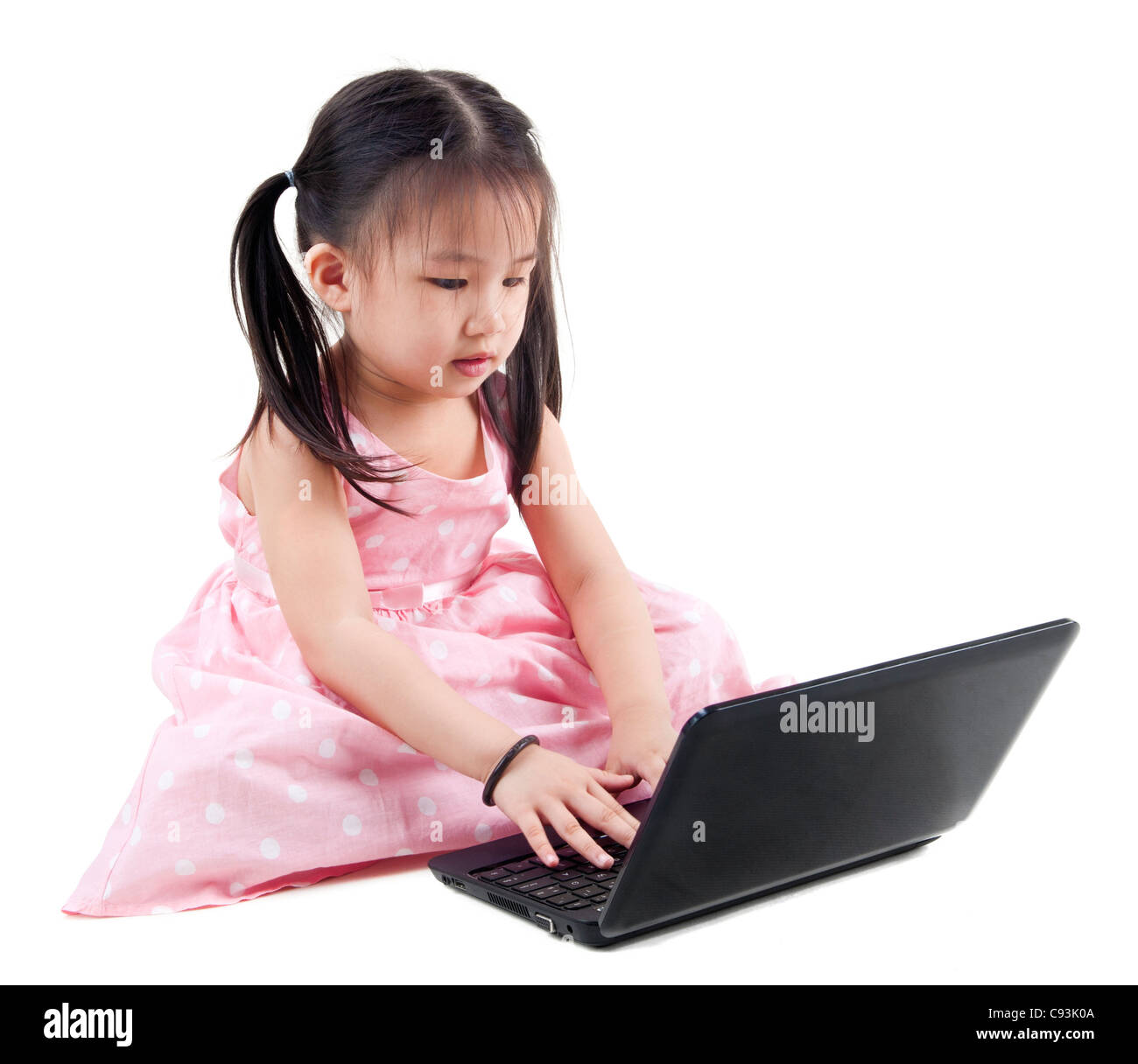 Belle petite fille assise sur le plancher à l'aide d'un ordinateur portable, fond blanc Banque D'Images