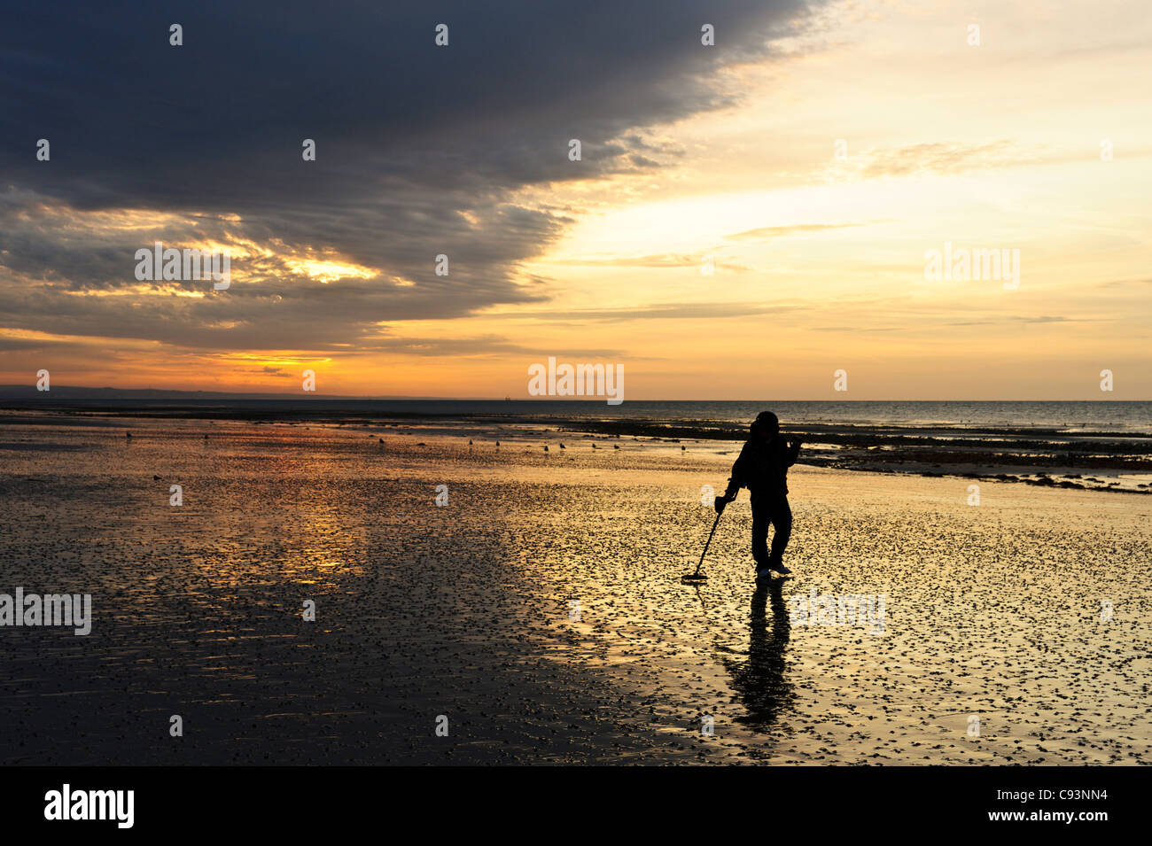 Un homme en peignant sur la plage de Worthing Beach en utilisant un détecteur de métal au lever du soleil. Banque D'Images