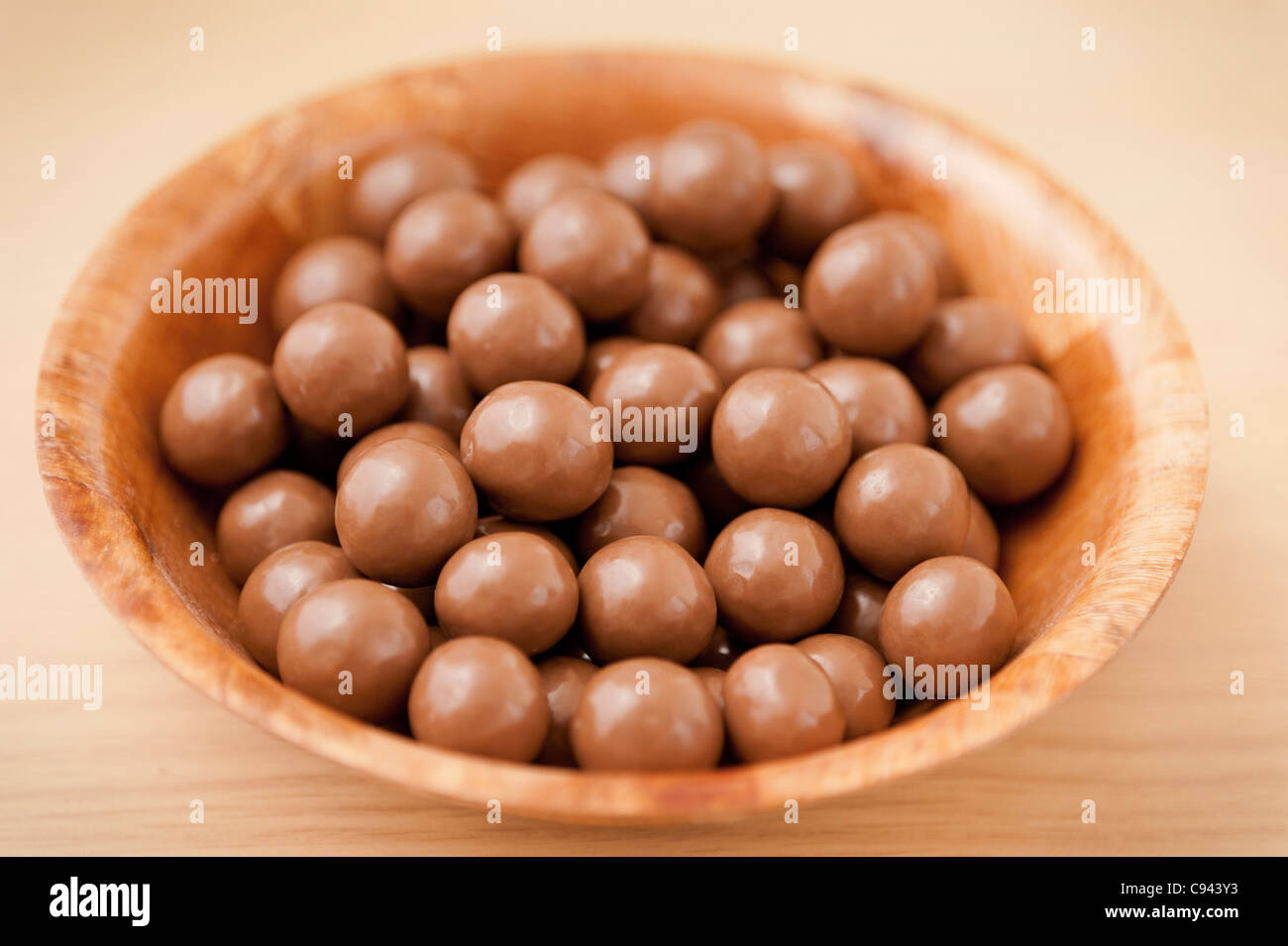 Détail d'un bol en bois contenant des billes de chocolat au lait délicieux sur une surface en bois Banque D'Images