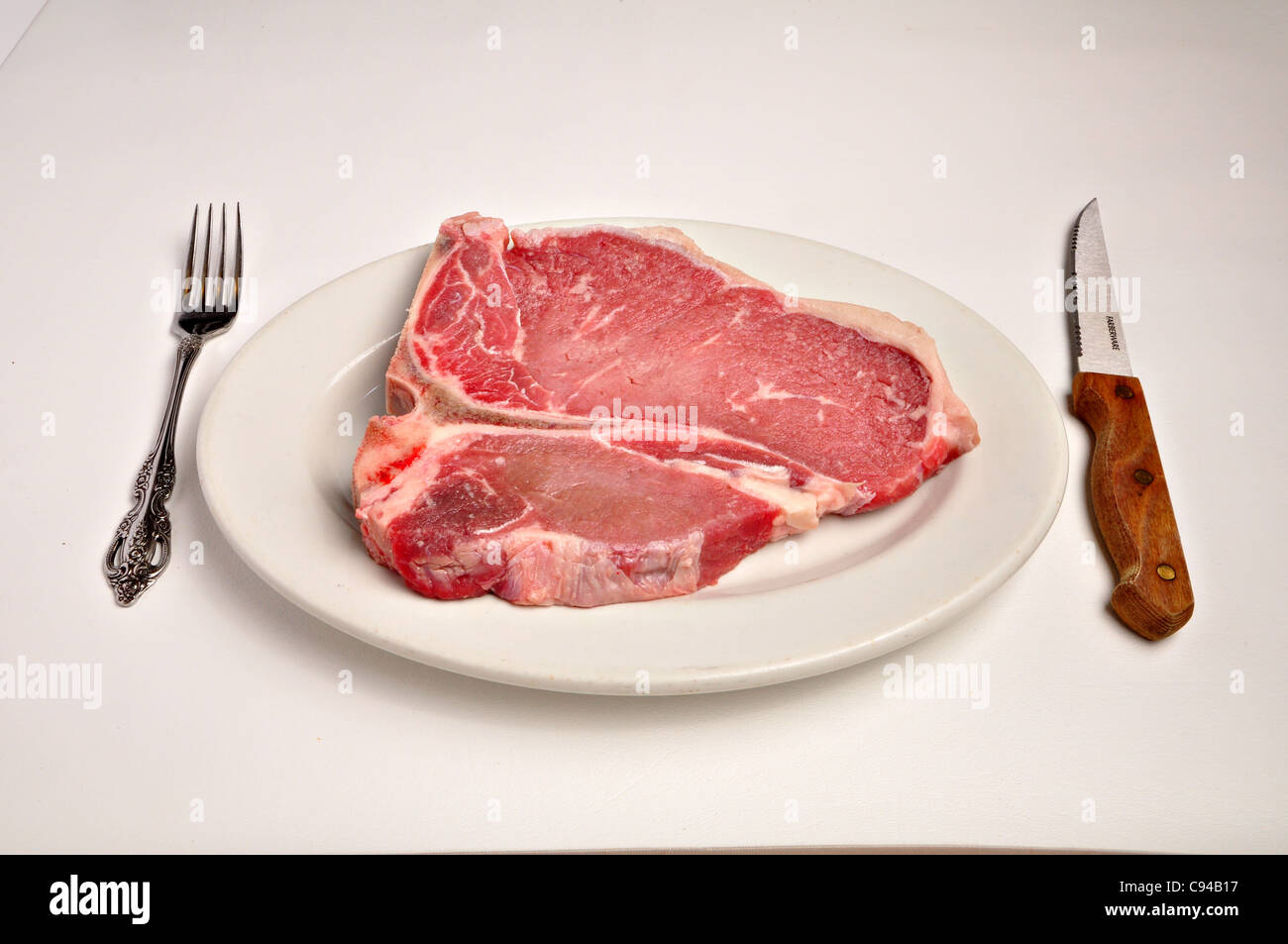 Une matière t-bone steak est posée sur une plaque blanche sur fond blanc. Banque D'Images