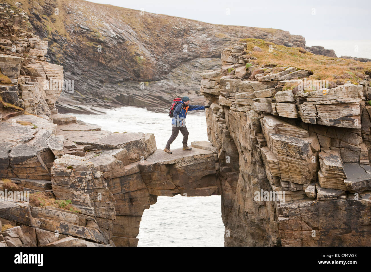 L'alpiniste traverse un pont de pierre cale qui relie les falaises d'une pile de la mer à Yesnaby sur la côte ouest des Orcades Banque D'Images