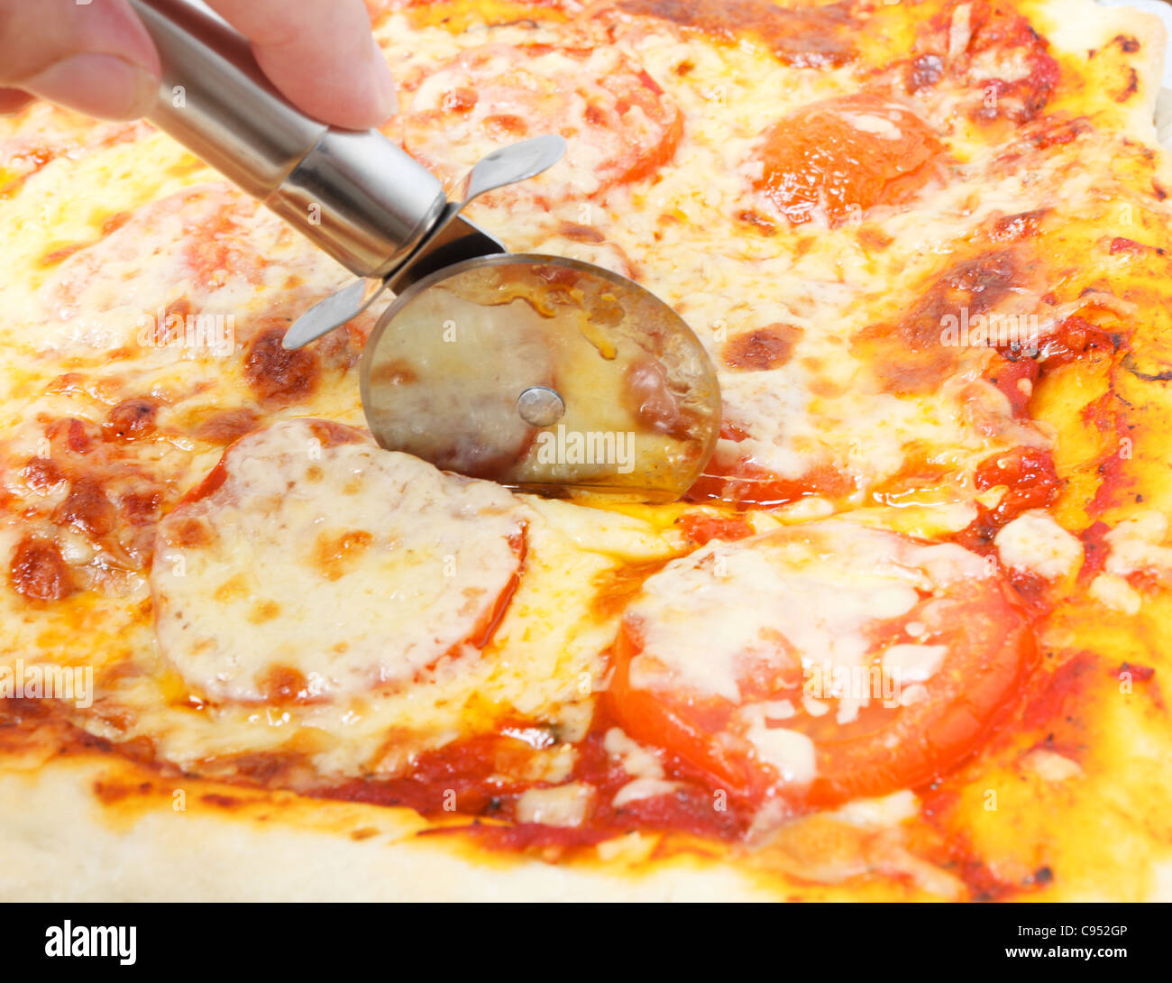 Couper un fromage et tomato pizza avec une roue à pizza Banque D'Images