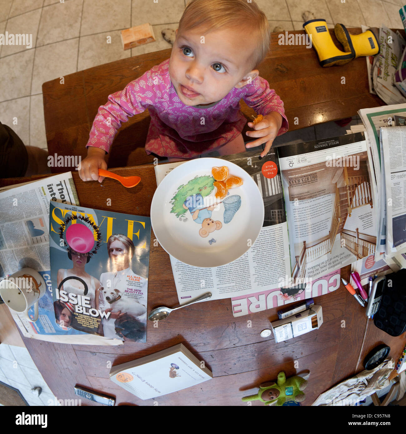 Fisheye Vue de dessus d'une petite fille mangeant les suprêmes d'orange à partir d'une plate entourée par les journaux du dimanche Banque D'Images