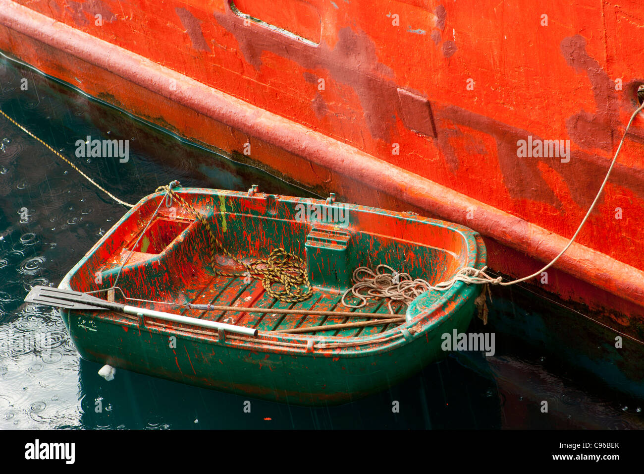 Petit bateau vert tendre / couvert de peinture orange et intégré à un grand navire peint en orange, sous la pluie, Banque D'Images