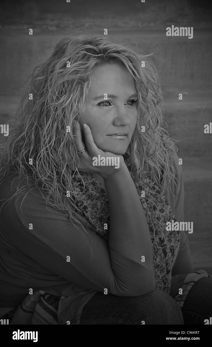 Cette jolie femme de race blanche à mi-vie est assis sur des escaliers de ciment à la recherche dans la distance avec une expression calme, paisible. Banque D'Images